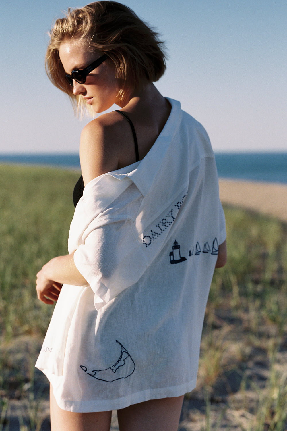 Woman wearing a white shirt with text and graphics, standing on a beach.