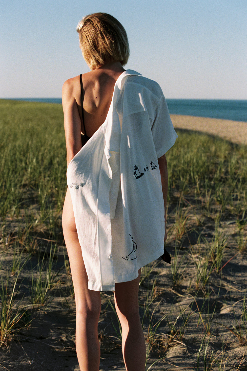 Person standing on a beach with a white shirt draped over their shoulders
