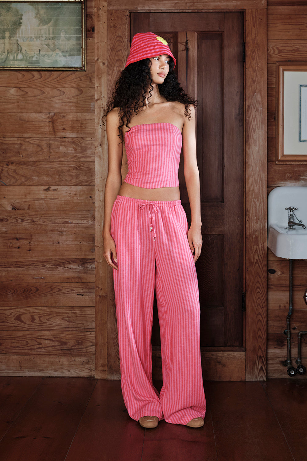 Woman wearing a pink outfit standing in a wooden interior setting.
|M1