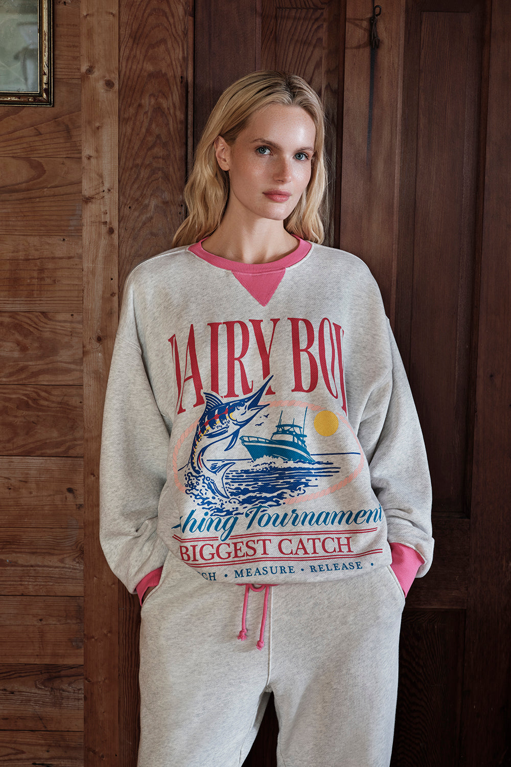 Woman wearing a 'Dairy Boy' sweatshirt with a fish graphic in a rustic setting
|M1