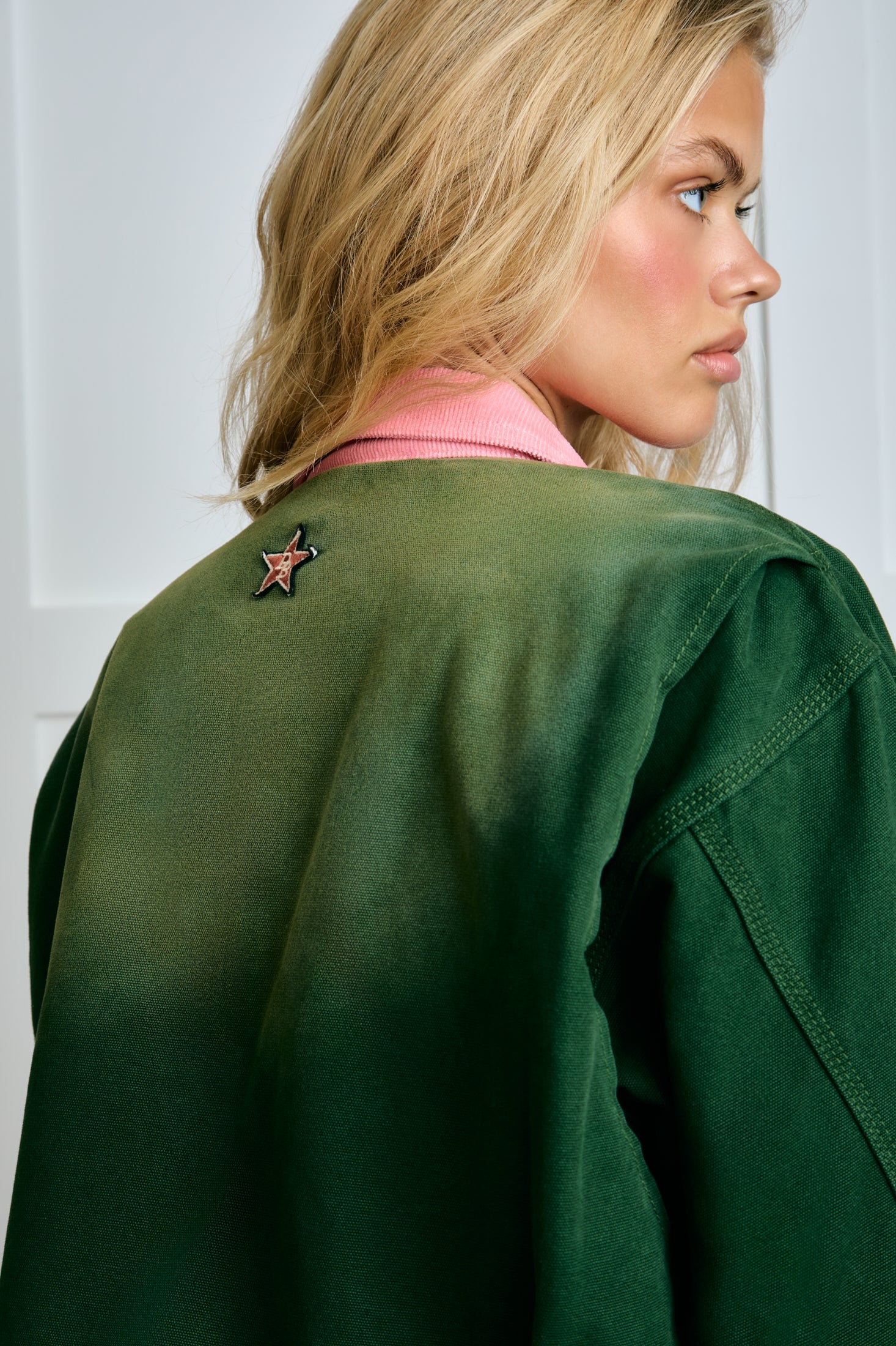 Person wearing a green jacket with a pink shirt underneath, against a plain background |m1