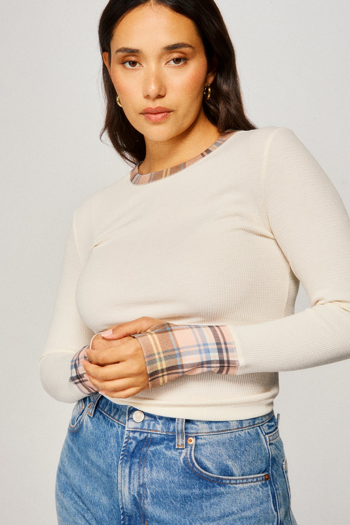 Woman wearing a cream sweater with plaid cuffs and hem against a plain background |m1