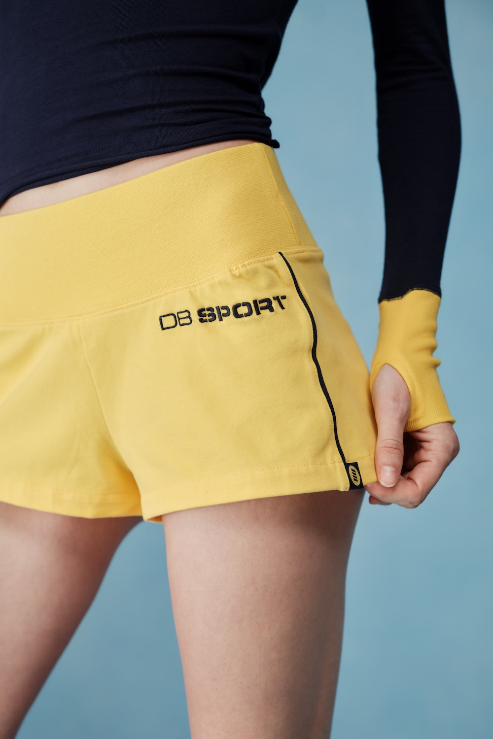 Person wearing yellow sports shorts with a brand logo on a blue background |M1