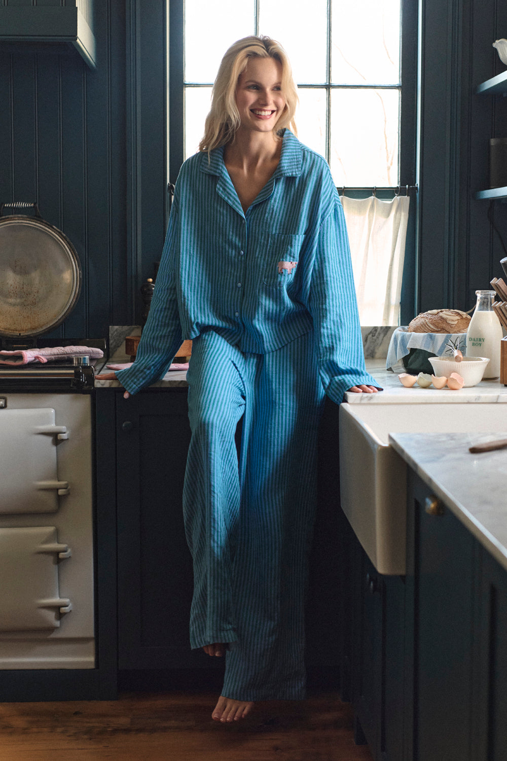Woman in blue pajamas standing in a kitchen. |M1