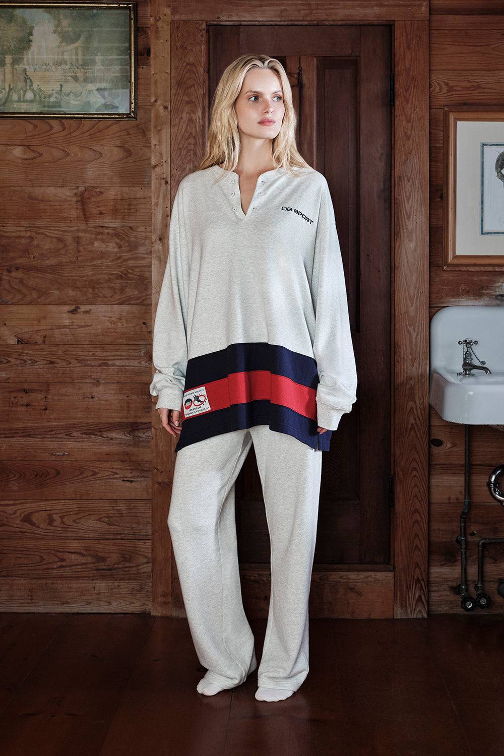 Woman wearing a white tracksuit with red and blue accents in a wooden interior setting.
|M1