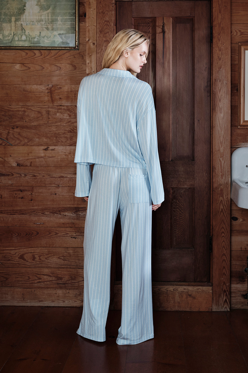 Woman in light blue ribbed top and pants standing in a room with wooden walls.
|M1