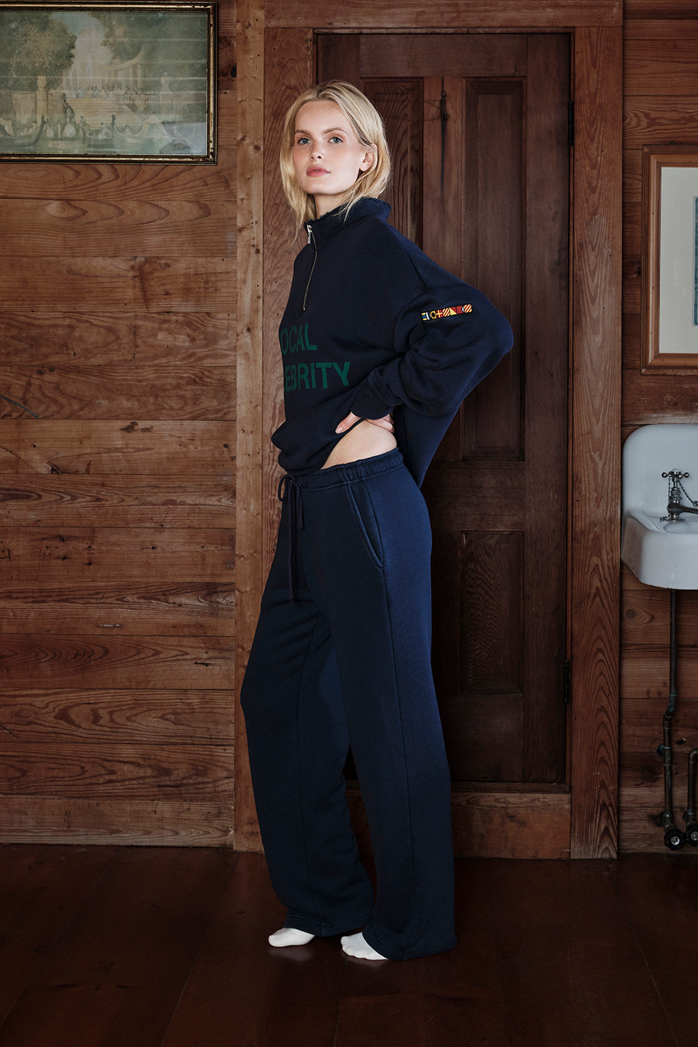 Woman in a navy blue outfit standing in a room with wooden walls.
|M1