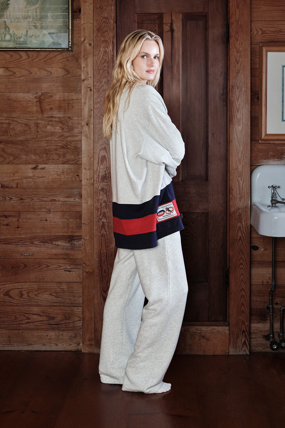 Woman in a white outfit with a colorful belt standing in a wooden interior.
|M1