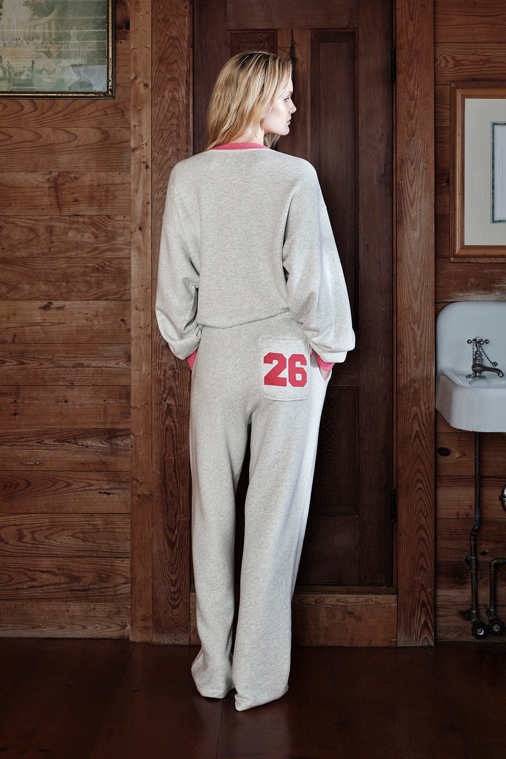 Woman wearing a gray tracksuit with red numbers in a wooden interior setting
|M1