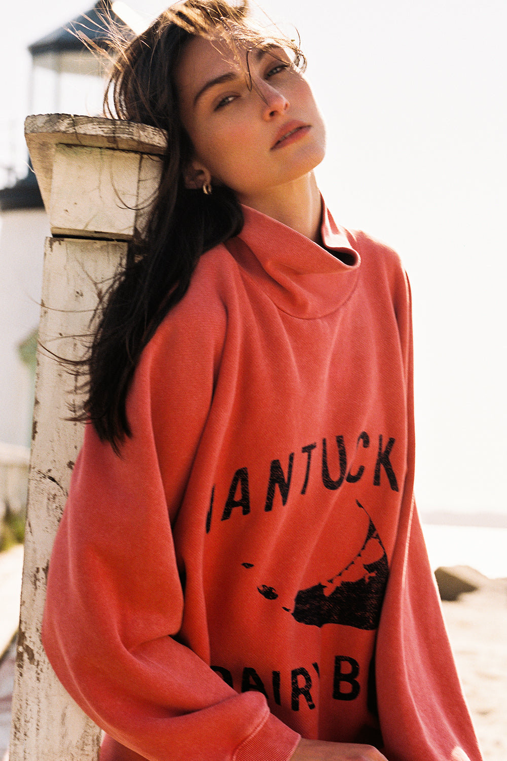 Woman wearing a red sweatshirt with text and graphics, leaning against a wooden post.