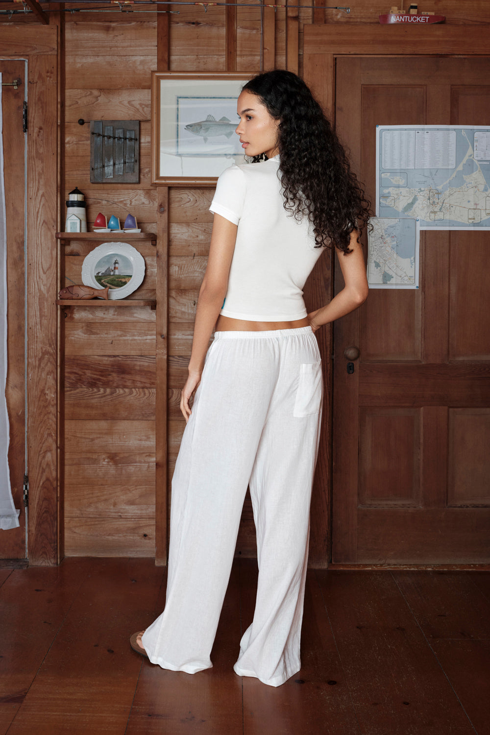 Woman in a white outfit standing in a room with wooden walls and decor.
|M1