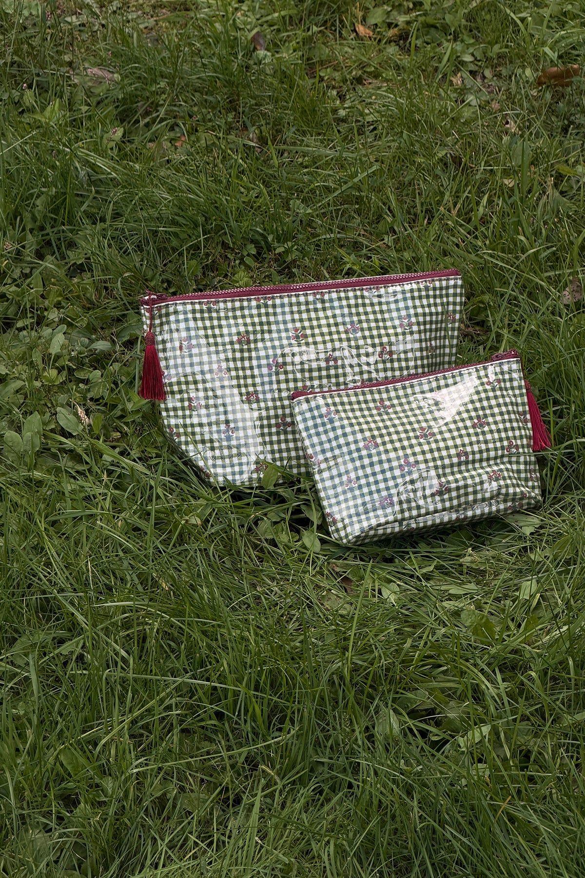 Two glossy green gingham zip pouches with small floral motifs and burgundy zips and tassels, shown together in different sizes.