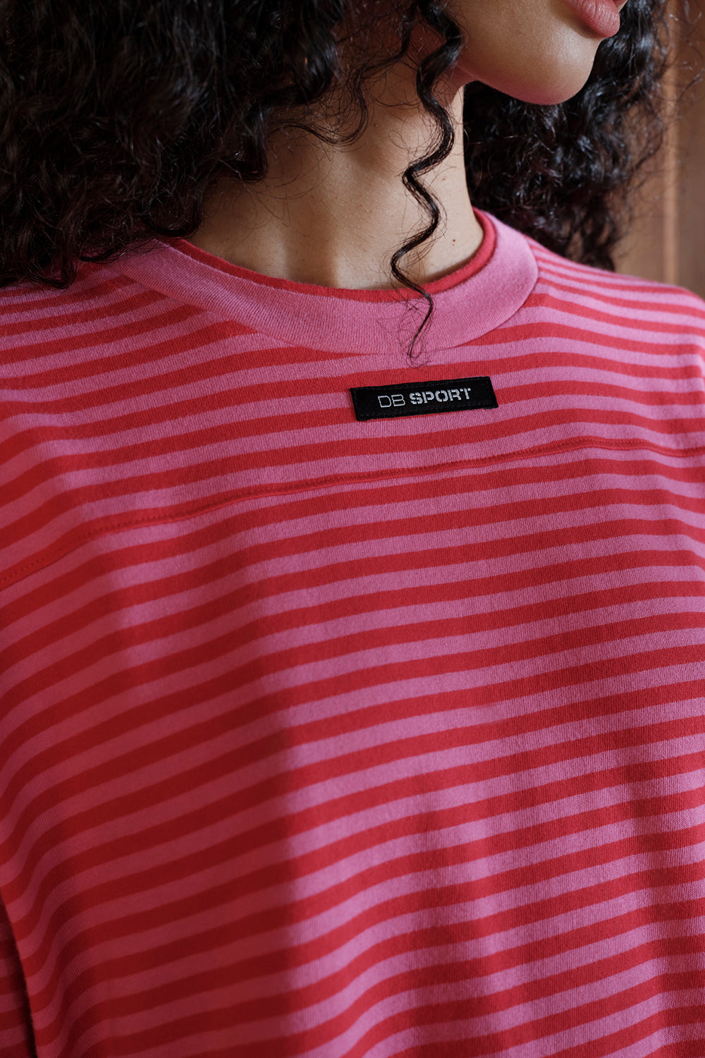 Person wearing a pink and white striped shirt with a brand label.
|M1