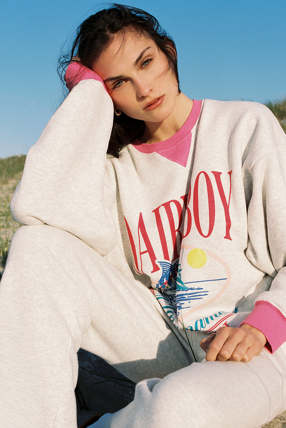 Woman wearing a 'Dairy Boy' sweatshirt with a colorful design, sitting outdoors.