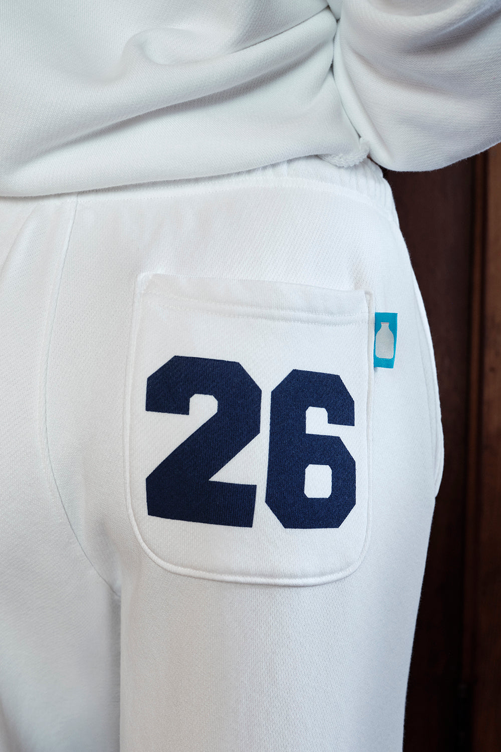 White pants with a pocket displaying the number 26 and a blue logo.
|M1