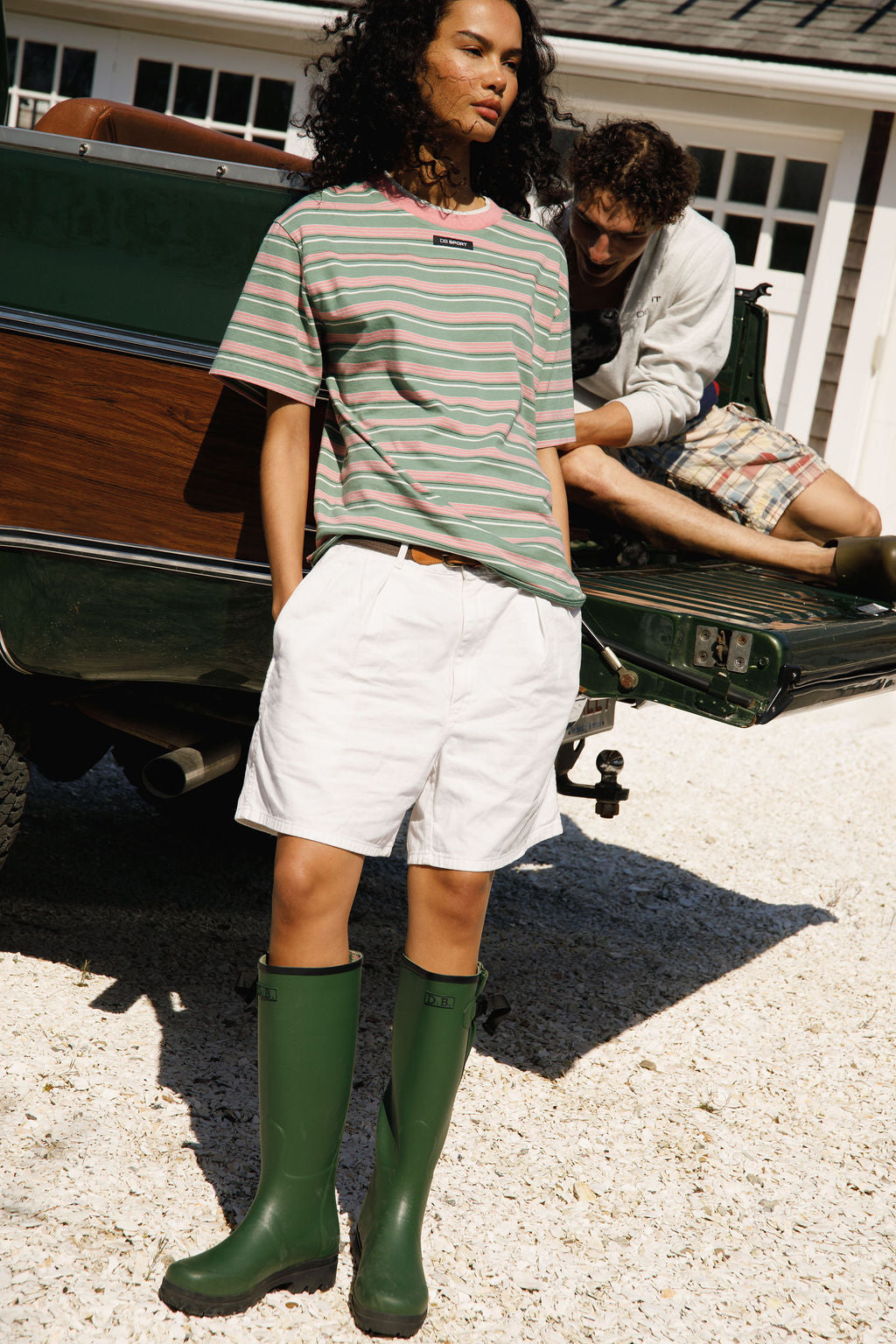 Person wearing a striped shirt, white shorts, and green rain boots standing next to a vintage truck.