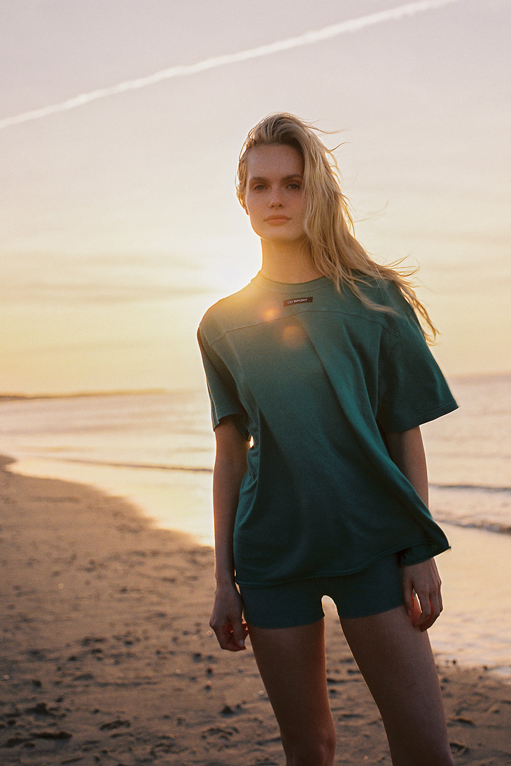 Woman in green outfit standing on a beach at sunset