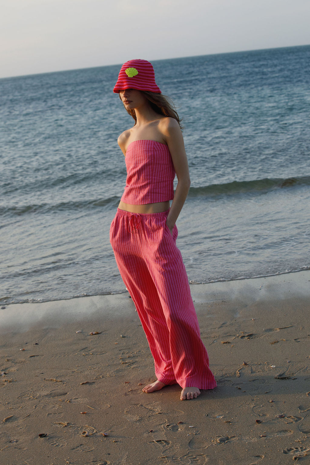 Woman in pink outfit standing on a beach with ocean waves in the background