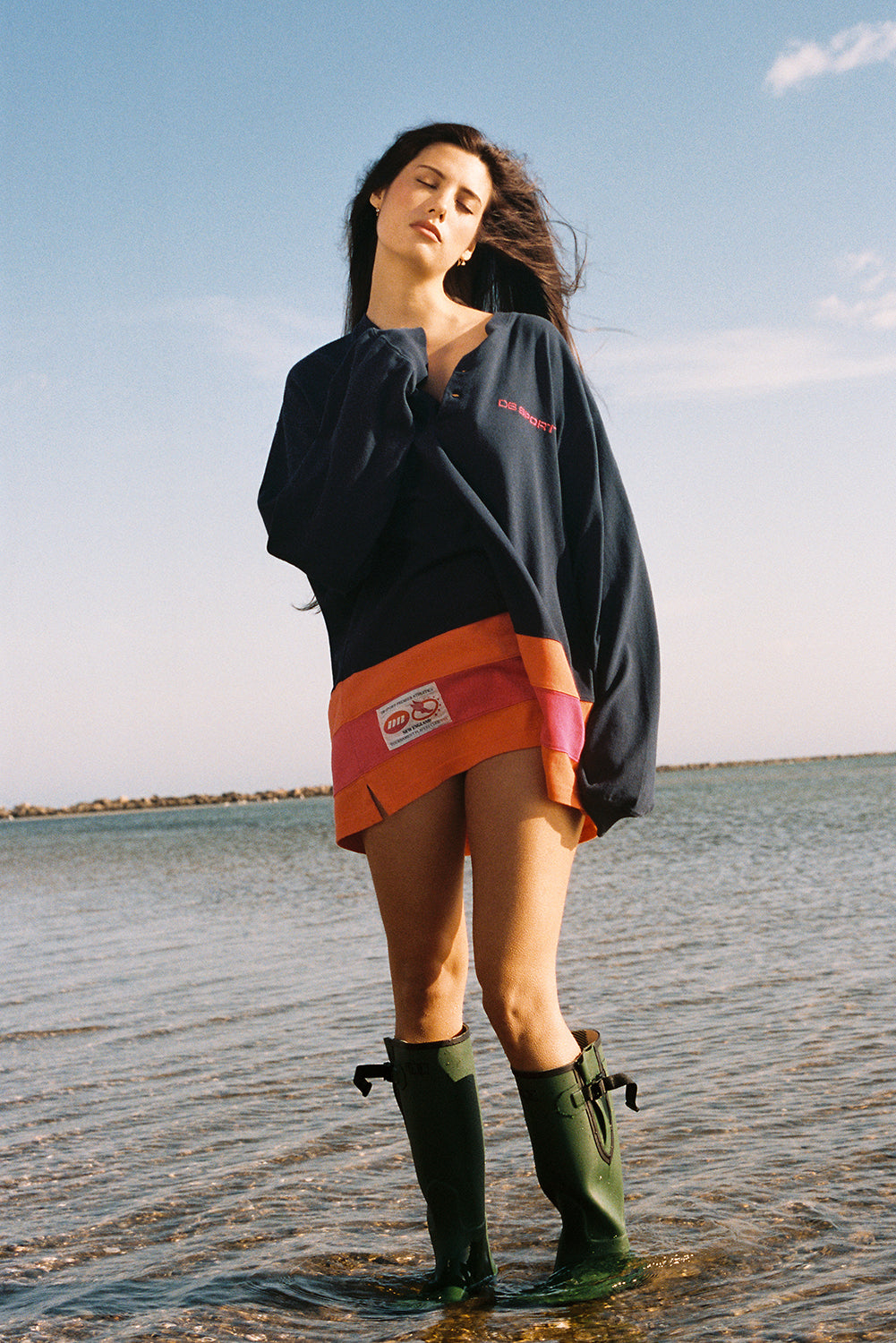Woman standing in water wearing a navy jersey, and green boots with a clear sky and water background.
|M2