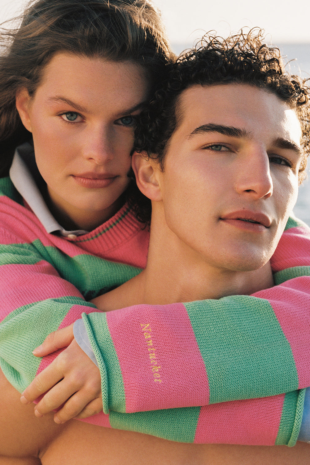 Two people hugging, one wearing a pink and green striped sweater with 'Ninety Percent' branding.