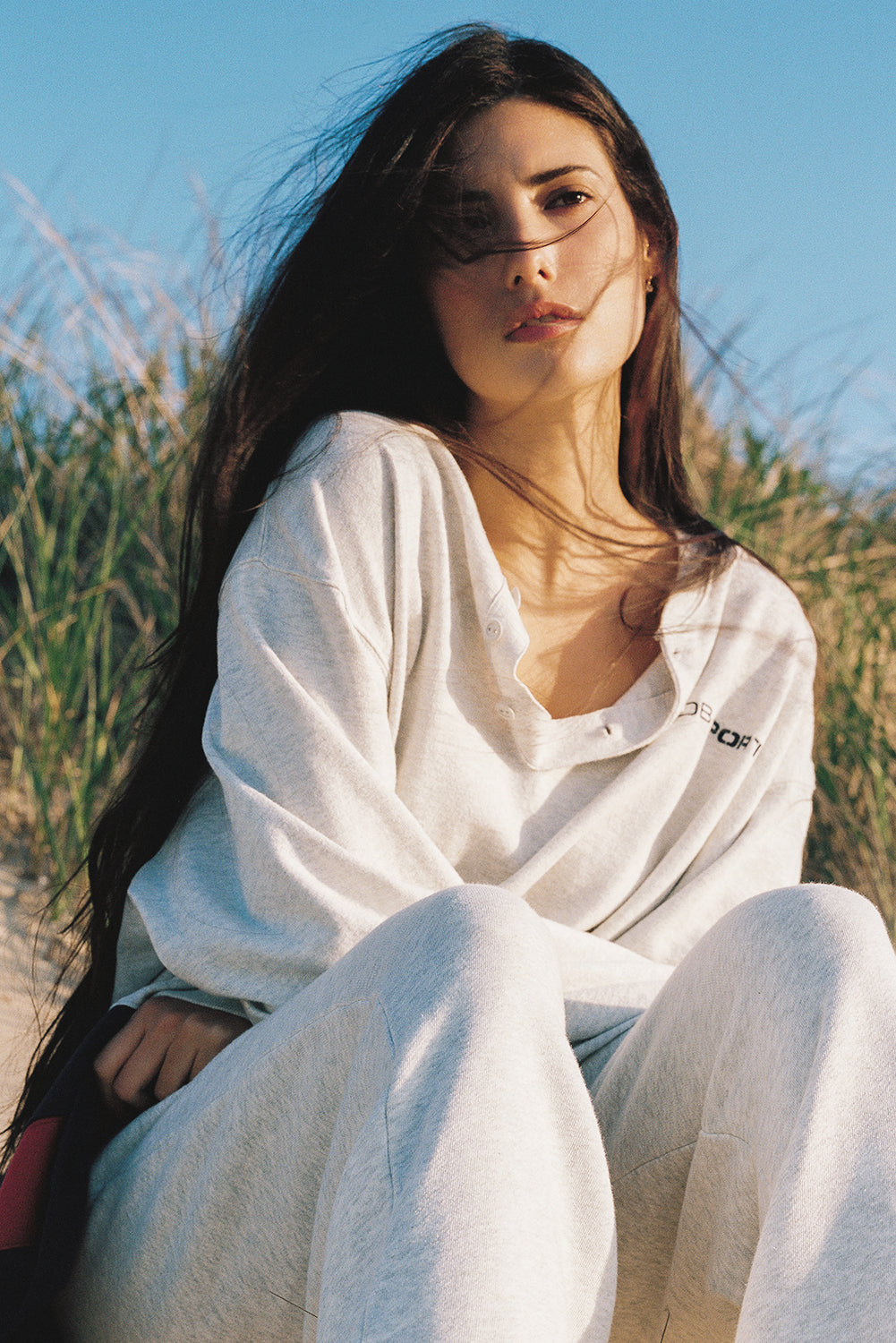 Woman in a white outfit sitting in a grassy field with a clear blue sky.
