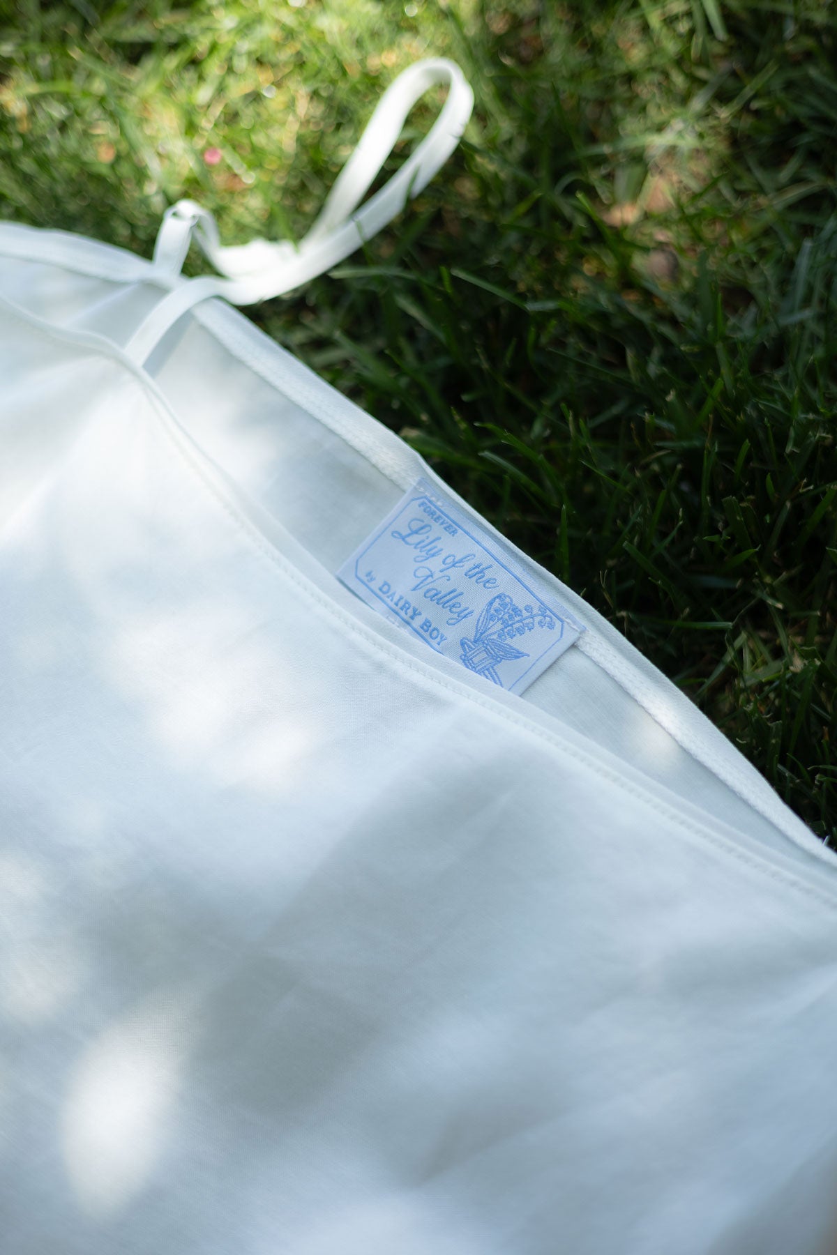 A close-up of a white garment laid on green grass, with a small blue-and-white brand label visible near the neckline.