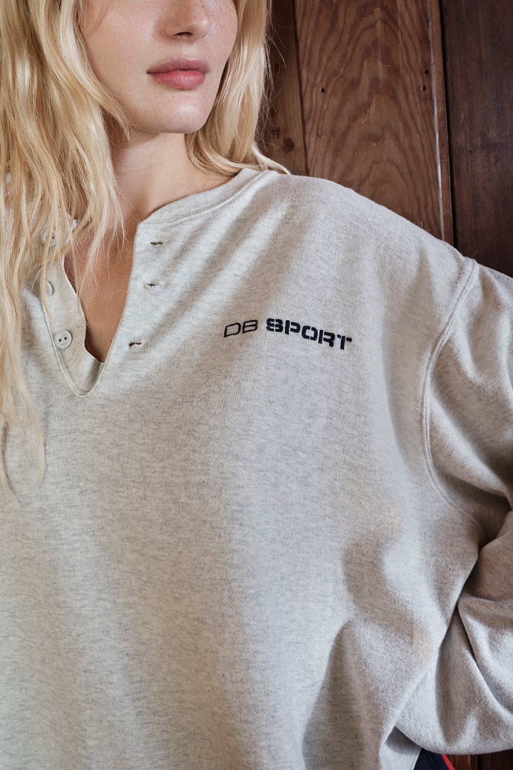 Person wearing a beige sweatshirt with 'DB Sport' logo against a wooden background