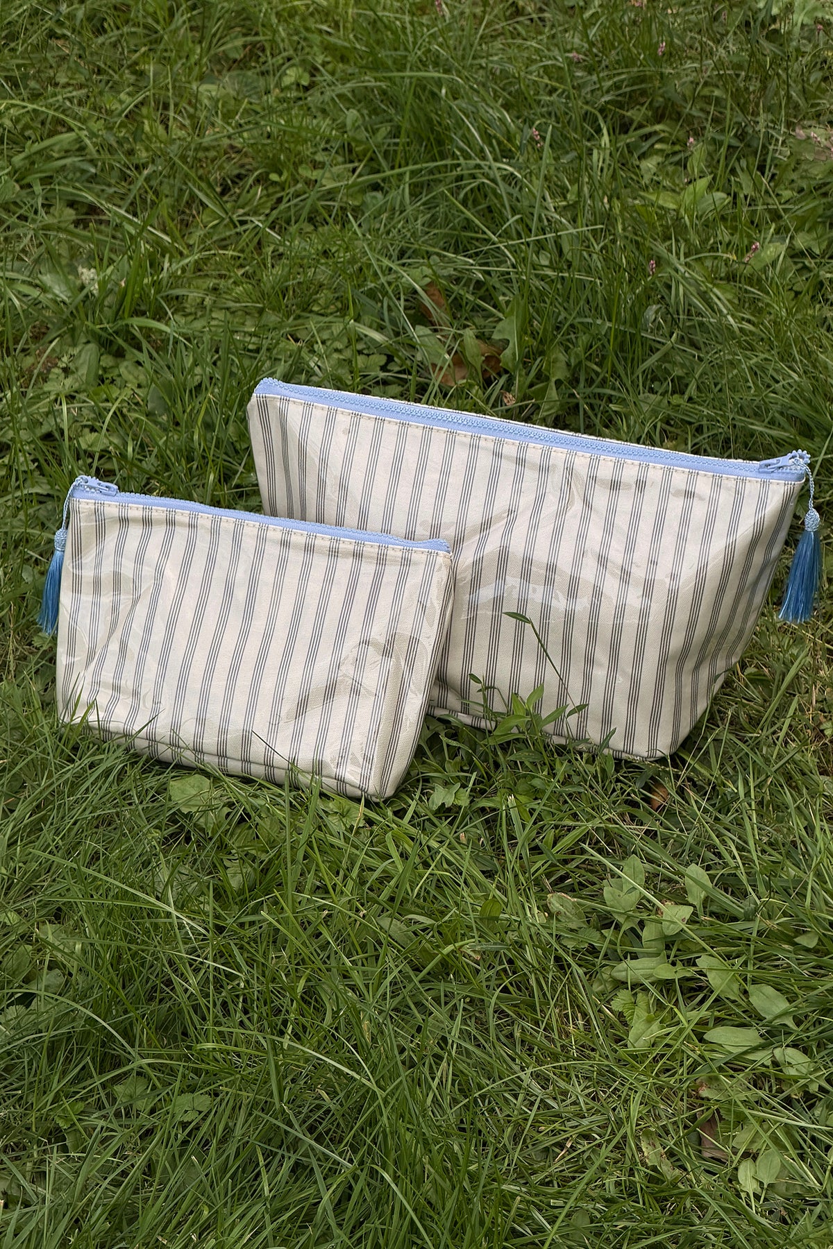 Two zip-top makeup bags in cream with thin brown stripes, light blue zips and blue tassel pulls, shown side by side.