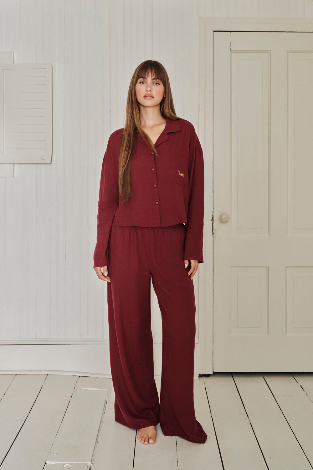 Woman wearing a burgundy pajama set in a room with a white door. |M1