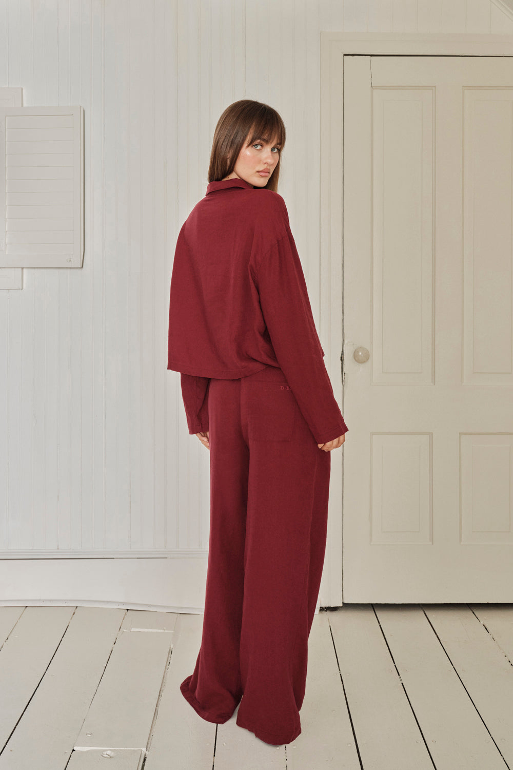 Person wearing a burgundy pajama set standing in a room with white walls and a door. |M1