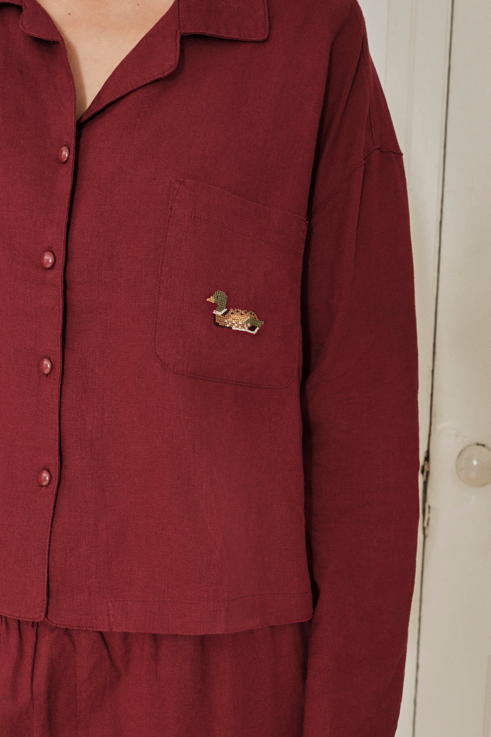Maroon pajama shirt with a small pocket and decorative button on a plain background. |M1