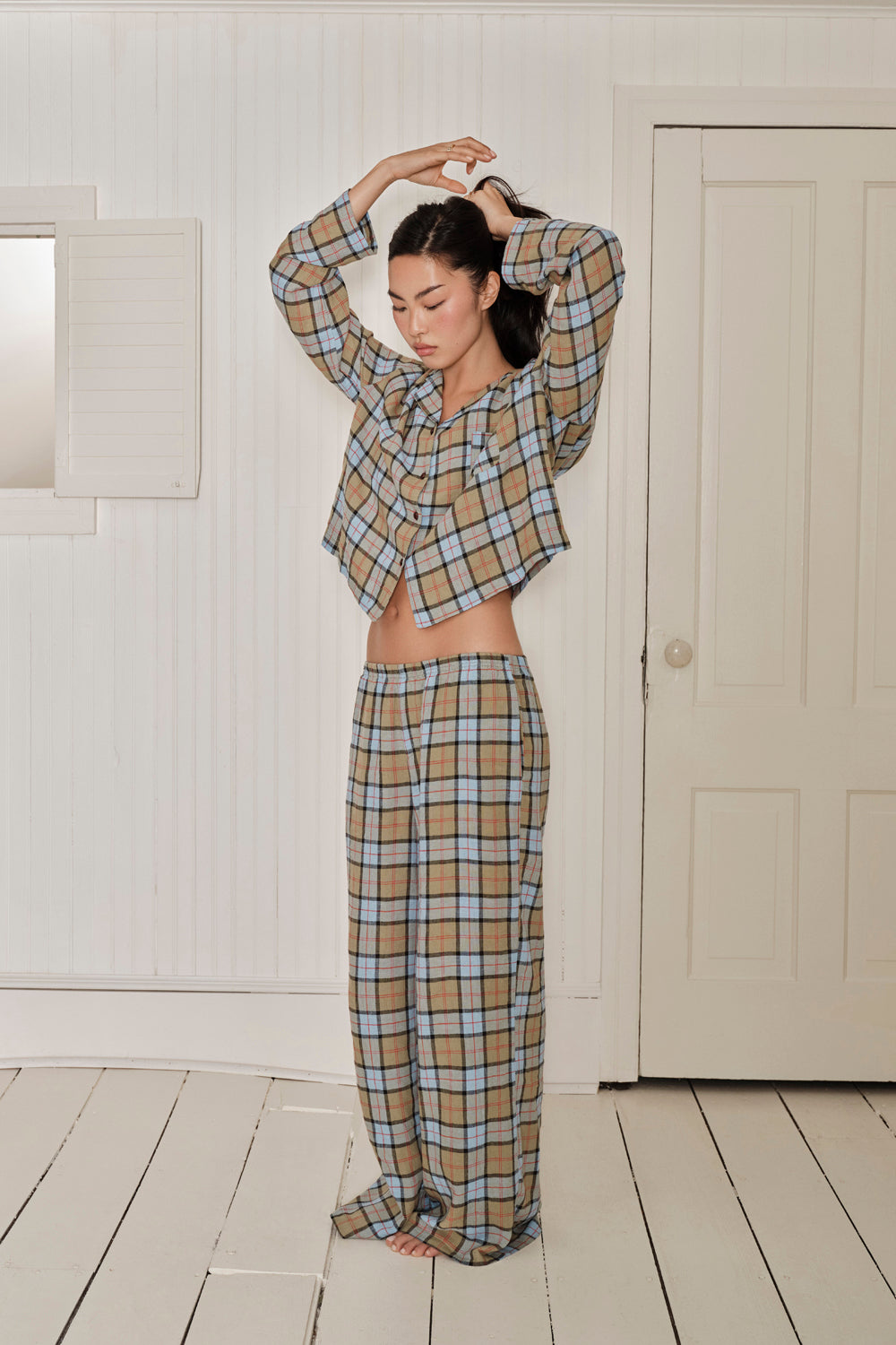 Person wearing a plaid outfit in a minimalistic room with white walls and wooden floor. |M1