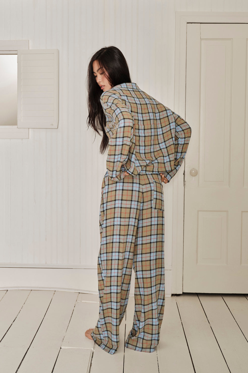 Person wearing a plaid outfit standing in a room with white walls and wooden floor. |M1