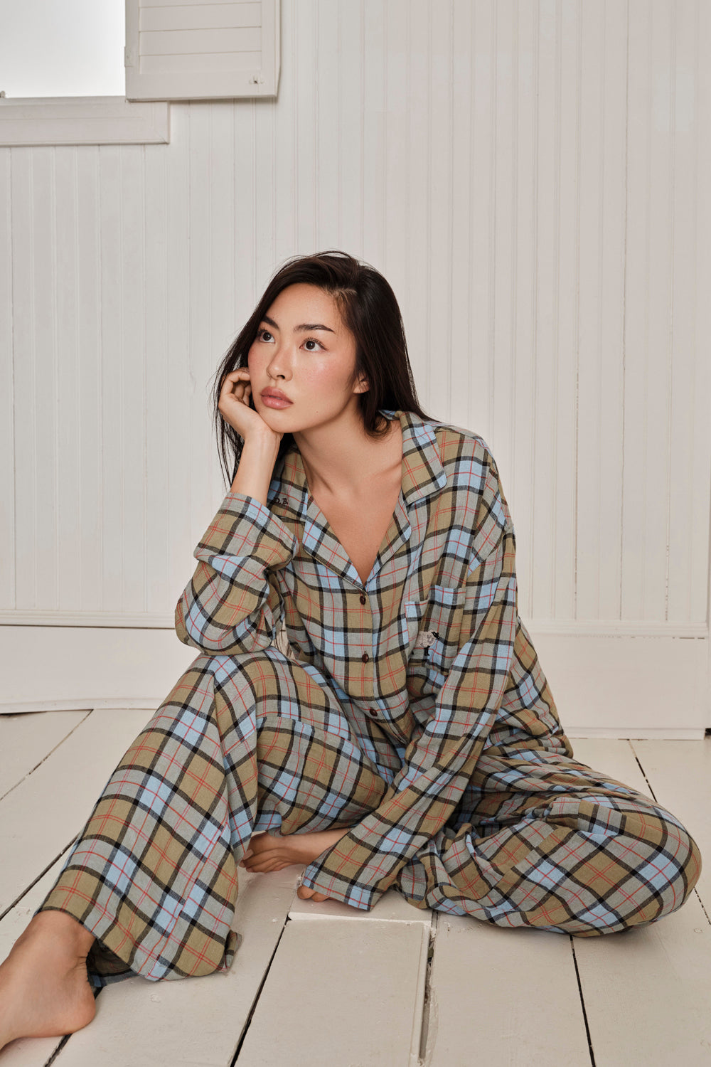 Woman wearing a plaid pajama set sitting on a wooden floor. |M1