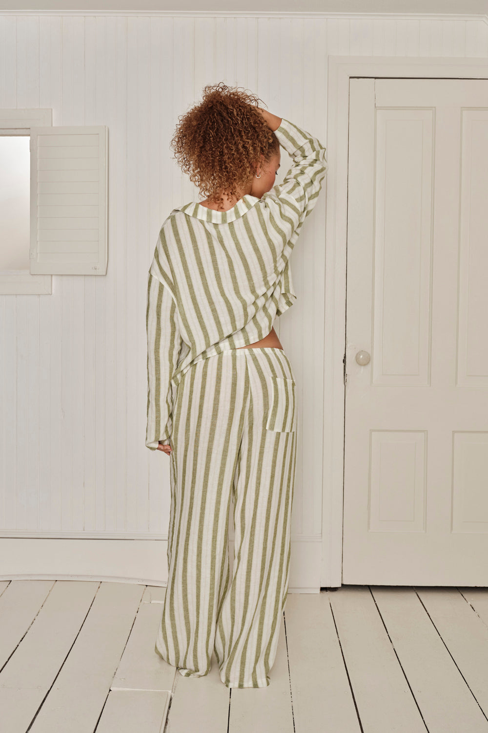 Person wearing a green and white striped pajama set in a minimalistic room. |M1