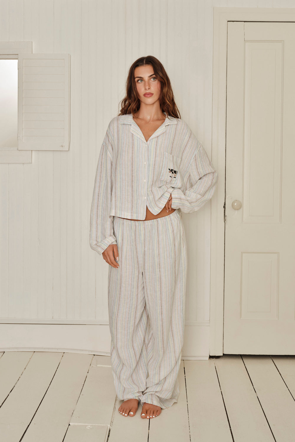 Woman wearing a striped shirt and pants in a minimalistic room with white walls and wooden floor. |M1