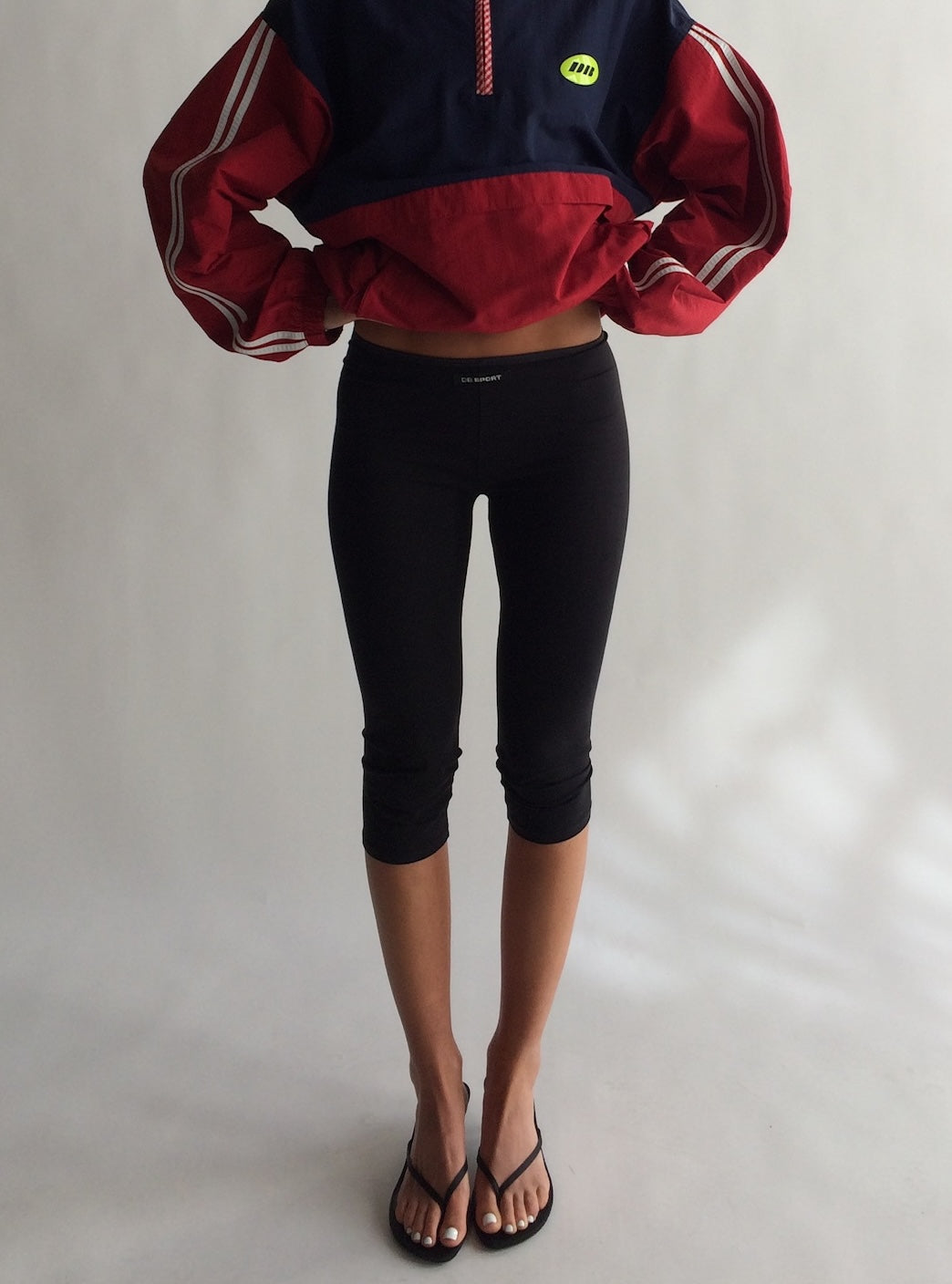 Person wearing a red and navy jacket with black capri pants on a plain background