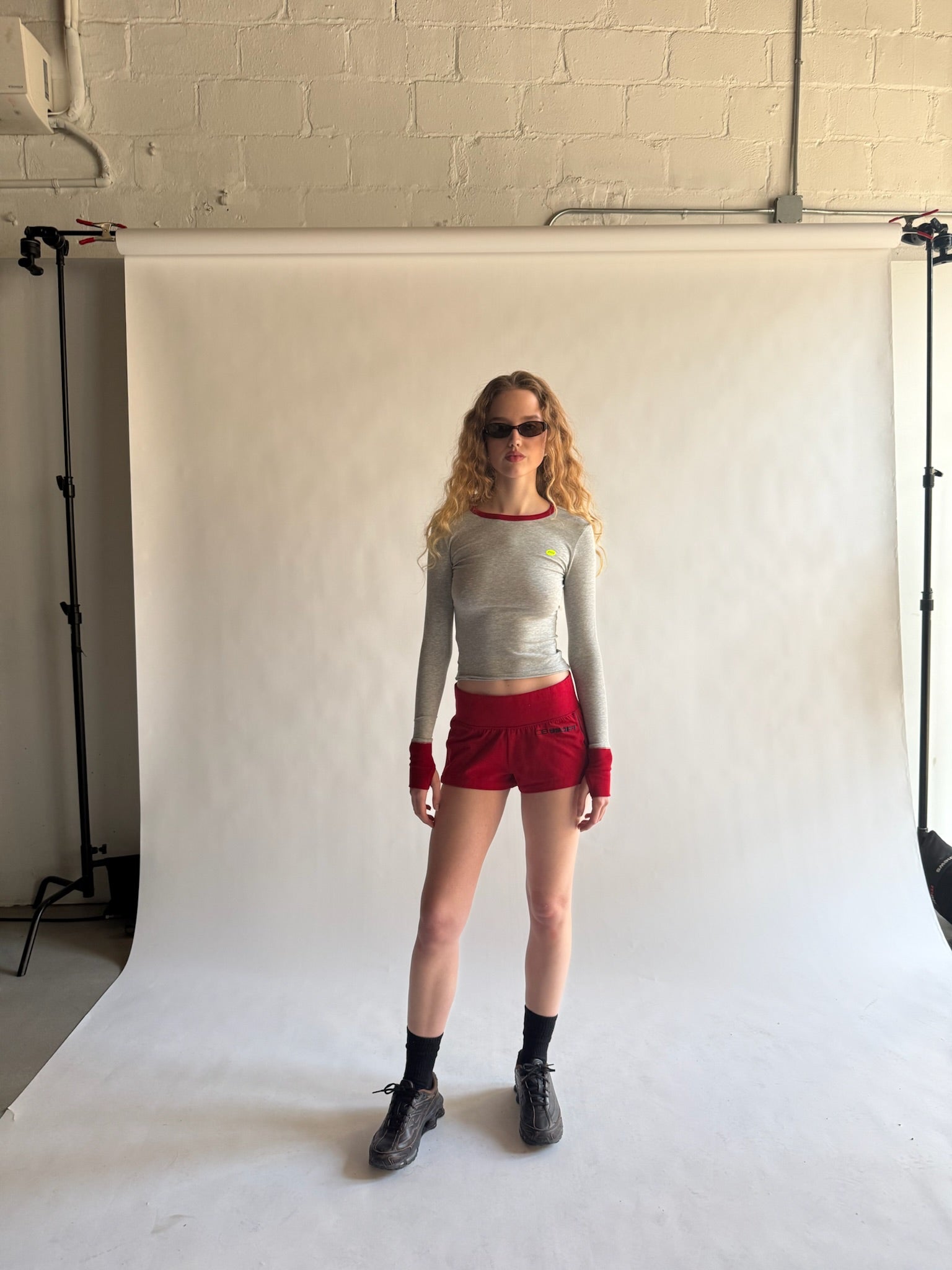 Person wearing a gray long-sleeve top and red shorts standing against a white backdrop. |M1