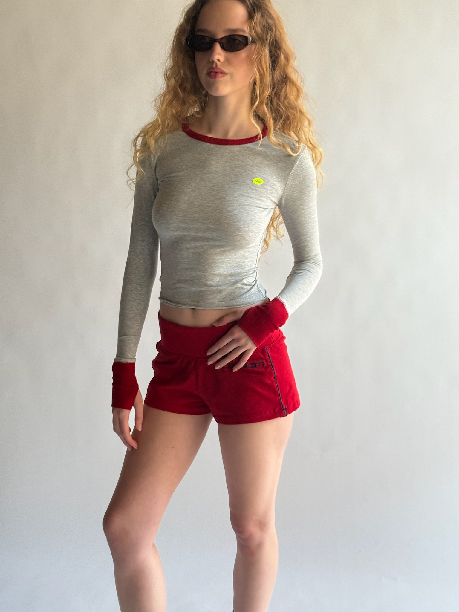 Person wearing a gray long-sleeve top and red shorts with a white background |M1