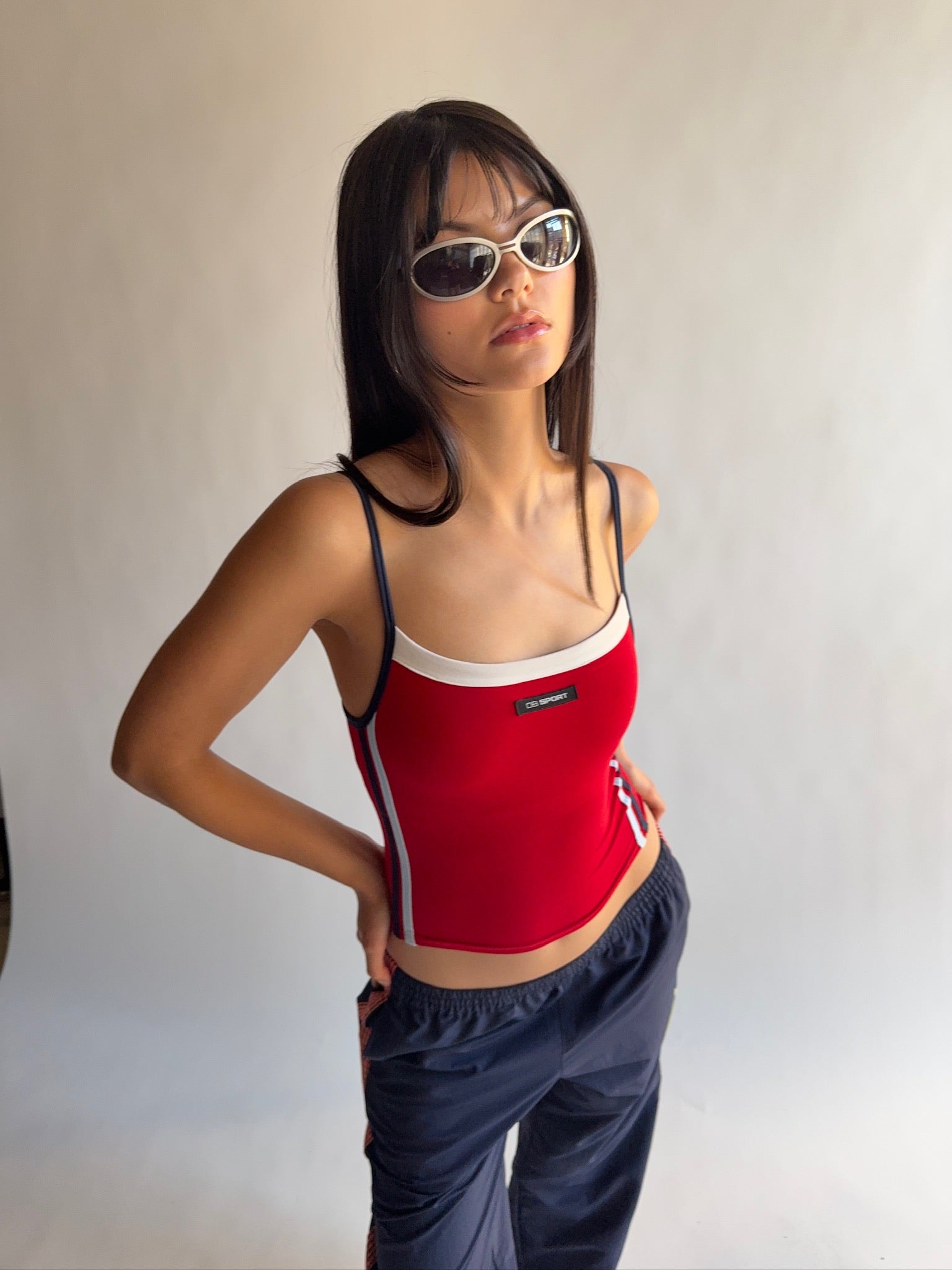 Person wearing a red tank top with a logo and dark pants against a plain background |M1