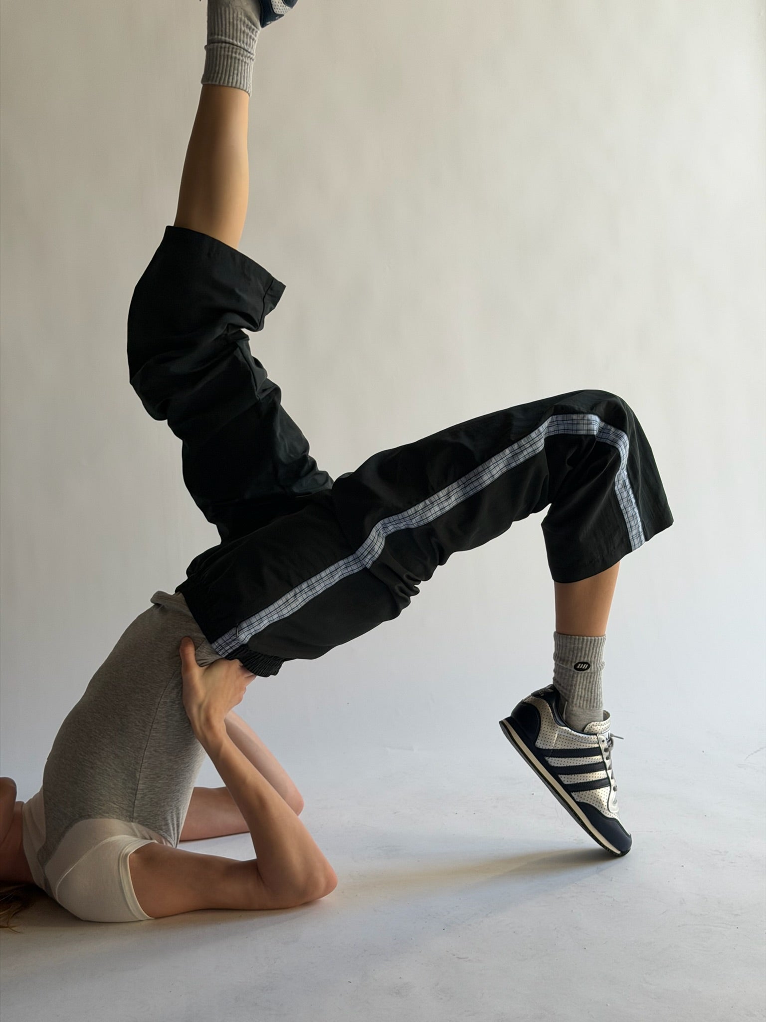 Person in black pants and shoes performing a handstand on a white floor.
