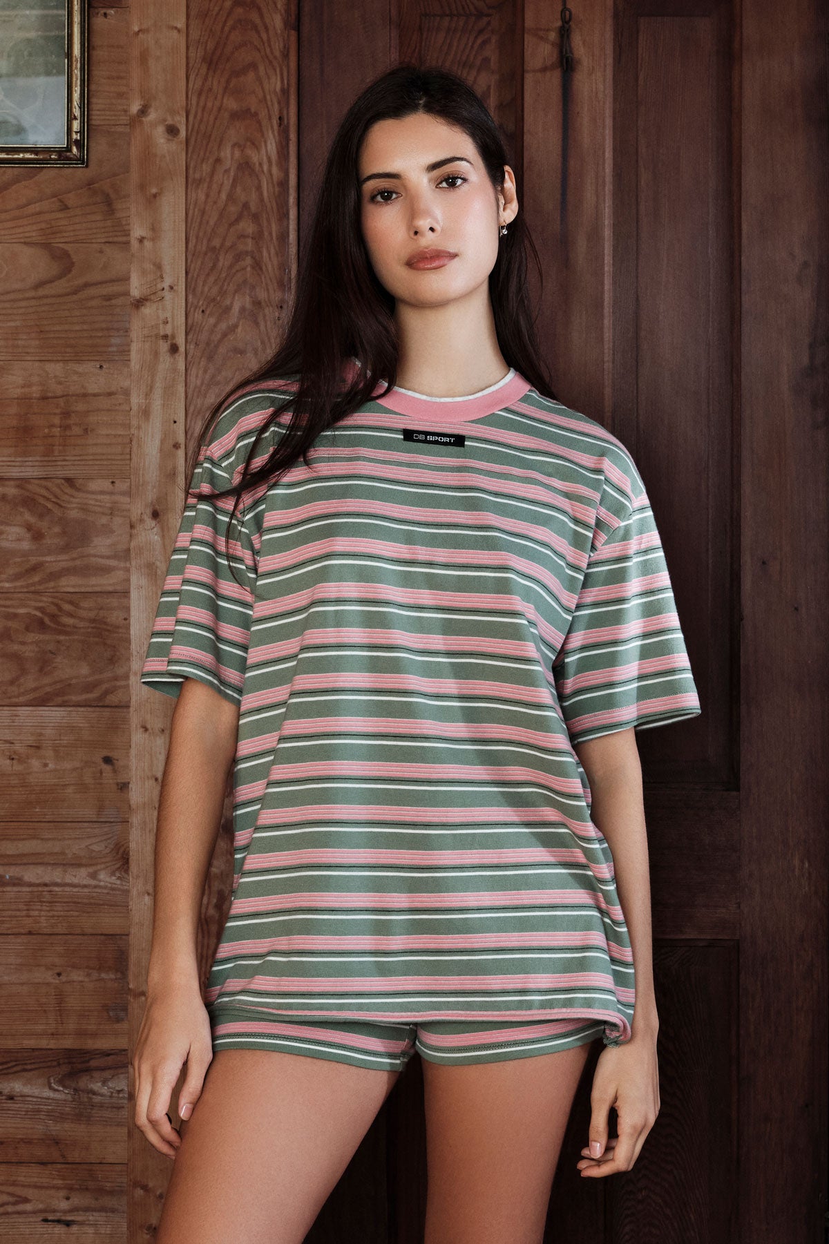 Woman wearing a striped shirt and shorts in front of a wooden wall
|M1