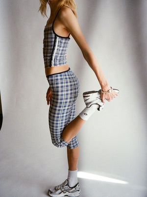 Person wearing a plaid outfit with a crop top and capri holding a sneaker against a plain background. |M1
