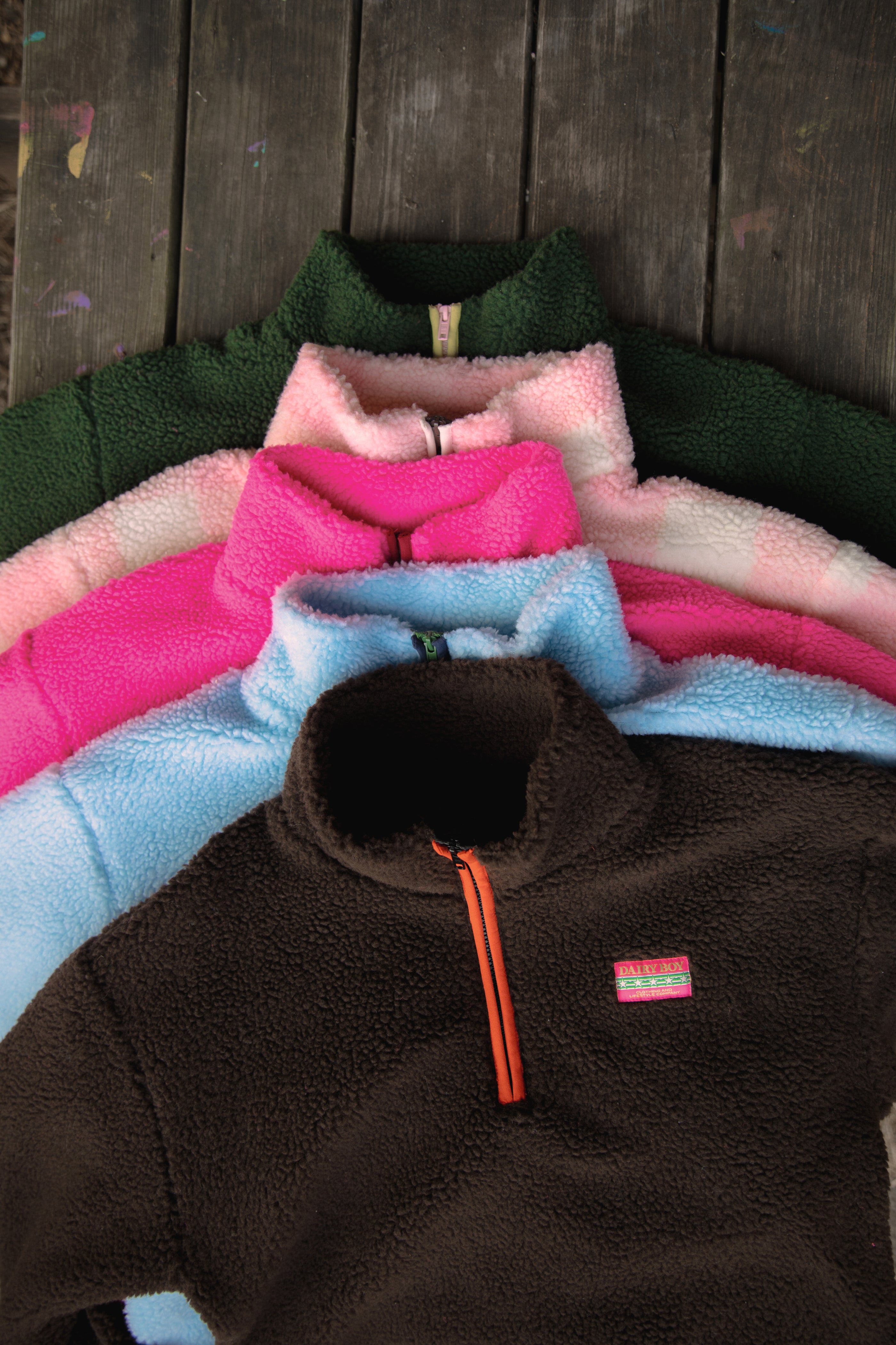 Stack of colorful fleece jackets with a brown one on top featuring a brand logo.