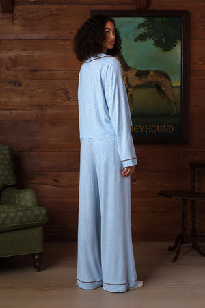 Back view on a model of a light blue pajama set with small dark dots, burgundy piping at the collar and cuffs, a wide-leg pant with back pocket and piped hem. |M1