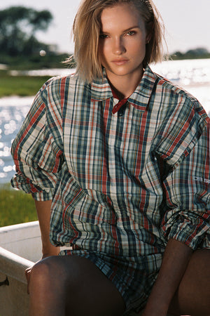 Woman wearing a plaid jacket sitting by a body of water.