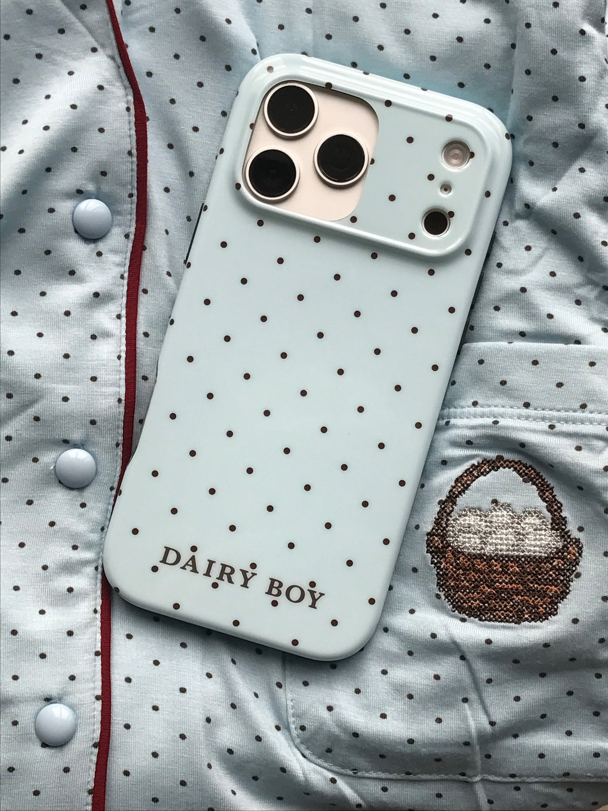 Pale blue phone case with scattered brown dots and "DAIRY BOY" lettering near the bottom, back view with a large camera cutout.