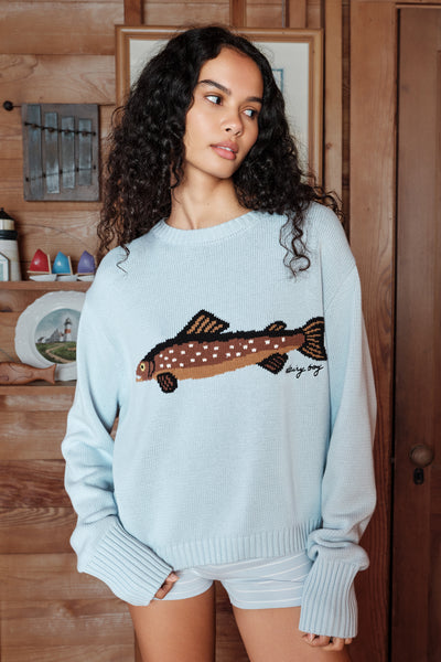 Woman wearing a light blue sweater with a fish design in a wooden interior setting 
|M1