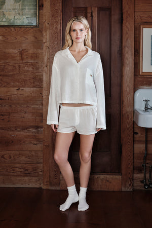 Woman wearing a white pajama shirt and shorts in a rustic wooden room.
|M1