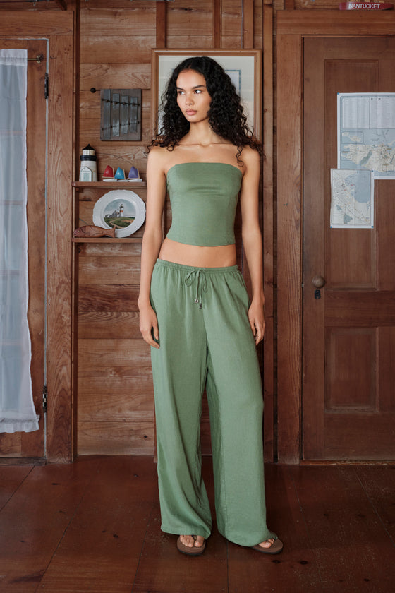 Woman wearing a green strapless top and wide-leg pants in a wooden interior setting.
|M1
